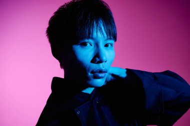 Şık bir Asyalı, kendine güvenen bir şekilde canlı bir neon arkaplan karşısında duruyor, benzersizliğini gösteriyor..