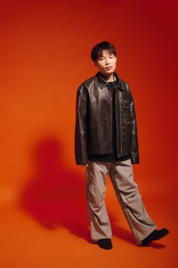 Şık bir Asyalı genç adam canlı turuncu bir arkaplan karşısında rahat bir şekilde poz veriyor..