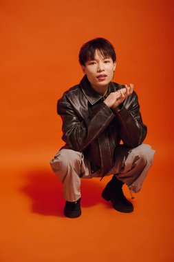 Yakışıklı genç bir adam modern giysiler içinde şık görünümünü sergileyerek çömeliyor..