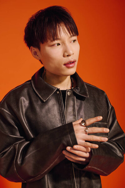 A handsome young Asian man confidently poses in a stylish leather jacket with an intense look.