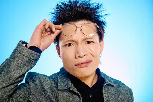 Симпатичный азиат демонстрирует любопытное выражение, настраивая очки в шикарном наряде..