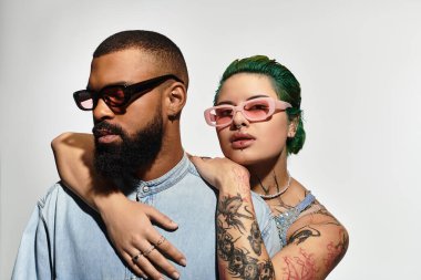 Şık bir çift, bir stüdyoda şık güneş gözlükleri ve canlı kıyafetler sergileyerek kendine güvenen pozlar veriyor..