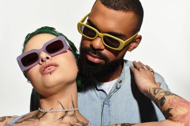 Moda bir çift şık güneş gözlükleriyle poz veriyor. Stüdyoda özgüven ve modern moda yayıyorlar..