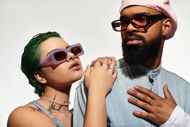 Şık genç bir çift stüdyoda birlikte poz veriyor, cesur güneş gözlükleri ve eşsiz giysiler sergiliyorlar..