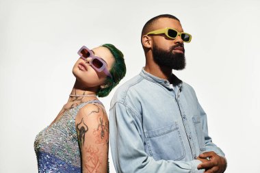 Genç çift, şık kıyafetler ve kalın güneş gözlükleriyle birlikte poz verirken güven yayıyor..