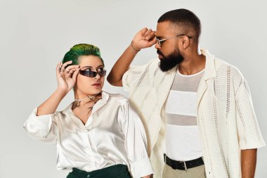 Genç çift, yaratıcı bir stüdyoda şık kıyafetler ve güneş gözlüğü takarak rahatça poz veriyor..
