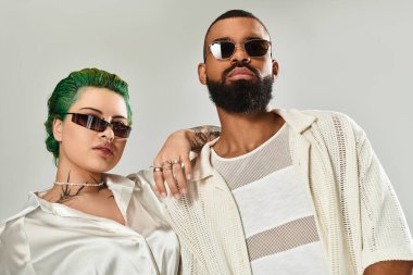 Şık bir çift stüdyoda kendine güvenerek poz veriyor. Benzersiz kıyafetler ve son moda güneş gözlükleri takıyorlar..