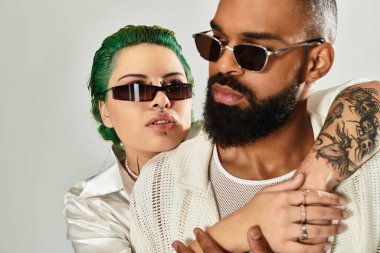 Modaya uygun bir çift, son moda güneş gözlükleriyle benzersiz tarzlarını yakın poz verirken sergiliyor..