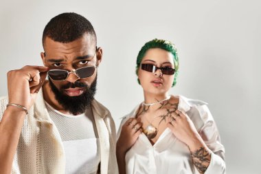 Şık bir çift stüdyoda, moda kıyafetler ve güneş gözlüğü takıp poz veriyor..