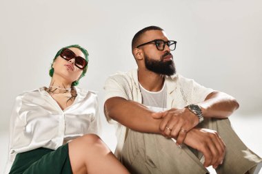 Moda sahibi bir çift stüdyoda güven içinde poz veriyor. Güneş gözlükleriyle tarz ve çeşitlilik yayıyorlar..