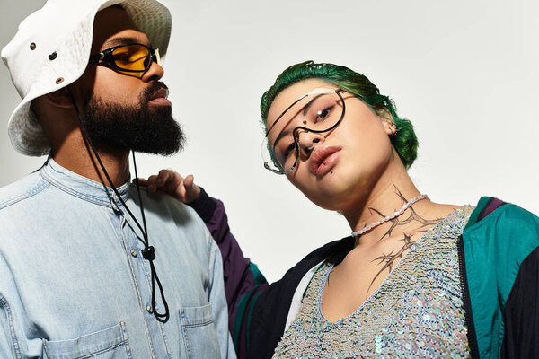 Модная мультикультурная пара уверенно позирует в студии в модных солнцезащитных очках.