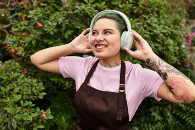 Gülümseyen bir kadın çiçeklerle ve çiçeklerle dolu canlı bir evde müzik dinlemekten hoşlanır..