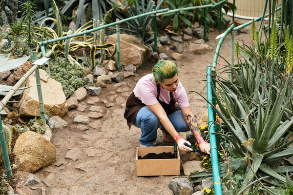 A young woman works diligently in a green house, nurturing plants and enriching the soil.