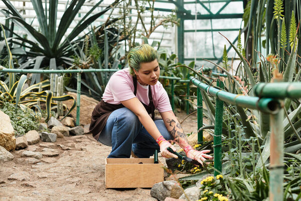 Dedicated young woman kneels in a lively greenhouse, nurturing plants with care and attention.