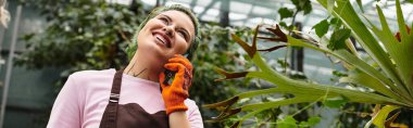 Canlı bir serada gelişen bitkilerle ustalıkla ilgilenirken gülümseyen genç kadın konuşuyor..