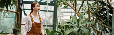 Güzel genç bir kadın renkli bir seranın içinde gelişen bitkilerle dolanıyor..