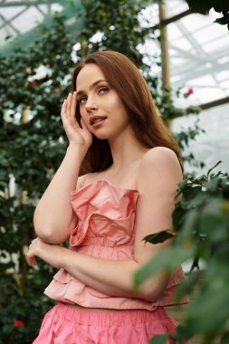 Genç ve güzel bir kadın zarif bir şekilde yemyeşil, ışık saçan cazibe ve sükunet arasında duruyor..