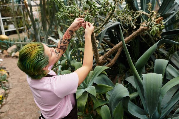 A young woman carefully arranges plants in a lush greenhouse filled with greenery and sunlight.