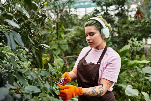 A young woman tends to plants in a vibrant greenhouse, pruning with care and focus.