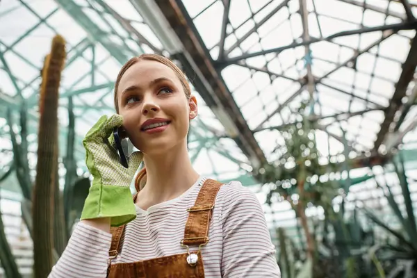 Genç bir kadın telefonuyla konuşuyor. Parlak, yeşil bir serada..