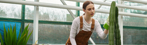 In a vibrant greenhouse, a young woman gently cares for a tall cactus, embracing nature.