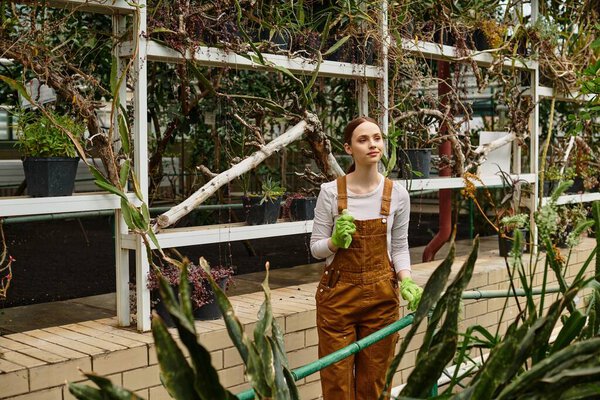 Bright eyed young woman lovingly tends to plants in a thriving greenhouse, surrounded by greenery.