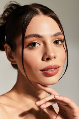 Genç bir kadın hafifçe izleyiciye bakıyor, nazikçe çenesine dokunuyor ve zarafet saçıyor..