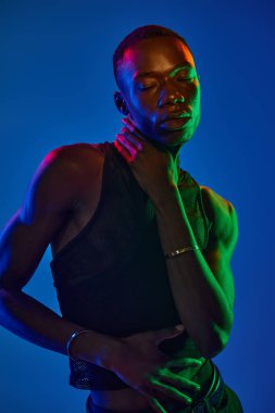 Genç bir Afrikalı Amerikalı, renkli ışıklandırmalarla çevrili şık kıyafetlere güveniyor..