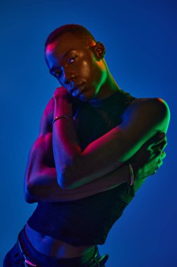 Şık giyinen genç adam renkli ışıkların altında rahatça poz veriyor..