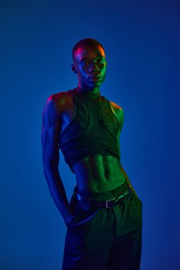 Kendine güvenen, Afro-Amerikan bir adam şık bir şekilde parlak ışıklarda duruyor, şehir modasını gözler önüne seriyor..