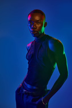 Genç bir Afro-Amerikan erkeği şık kıyafetler sergiliyor, canlı ışığa güven yayıyor..
