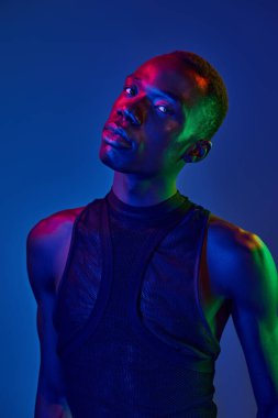 Genç bir adam yenilikçi kıyafetler giyer, çarpıcı renkli bir arkaplan karşısında kendine güvenir..