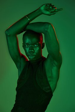 Şık bir genç adam canlı yeşil ışıklar altında kendine güvenerek poz verir. Sanatsal ve davranışsal özellikleri somutlaştırır..