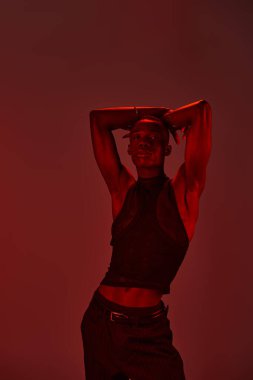 Genç bir Afro-Amerikan erkeği kendine güvenerek poz veriyor. Parlak kırmızı bir arka plana karşı..