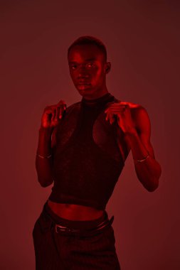 Afro-Amerikalı genç bir adam canlı kırmızı ışıklar altında şık giyimli modeller..