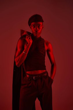 Genç Afro-Amerikan bir adam canlı kırmızı bir ortamda kendine güvenerek poz veriyor, şık kıyafetini gösteriyor..