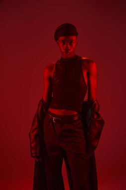 Kendine güvenen genç adam çarpıcı bir kırmızı arka plana karşı durarak modern kıyafetle cazibesini sergiliyor..