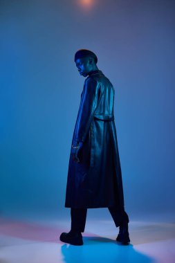 Genç bir adam, canlı bir arka plana karşı çarpıcı bir pozla moda anlayışını sergiliyor..