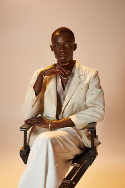 Kendine güvenen, şık giyinmiş Afro-Amerikan bir adam canlı bir stüdyoda oturuyor..