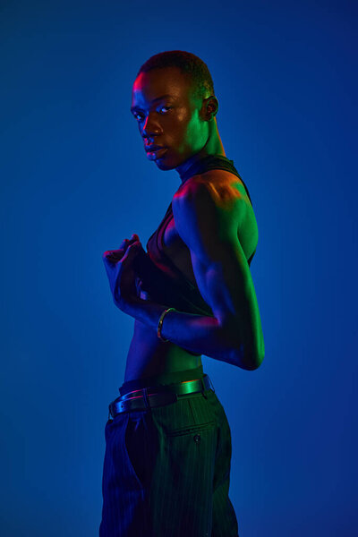Уверенный молодой африканский американец позирует в ярком одеянии, купаясь в ярких огнях.