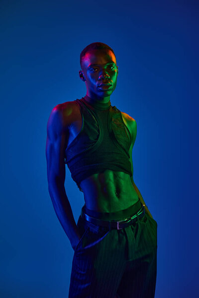 Уверенный молодой африканский американец стильно стоит в ярком свете, демонстрируя городскую моду..