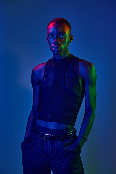 Стильный молодой африканский американец уверенно стоит, освещенный яркими огнями, демонстрируя свой стиль.