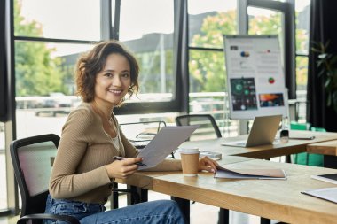 Kendini işine adamış biri, ekranlar ve kaynaklarla çevrili, parlak bir ofiste çok çalışır..