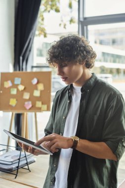 Genç bir profesyonel, canlı bir ofis atmosferiyle çevrili tabletlerine dikkatle odaklanır..