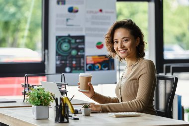 İyi organize olmuş bir ofis masasında kahve fincanıyla otururken profesyonel gülümsemeler..