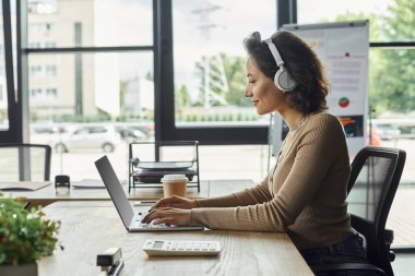 Parlak bir ofis alanında, kendini işine adamış bir profesyonel, kulaklık takıyor..