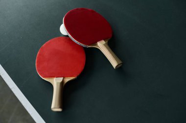İki ping pong raketi yeşil bir masanın üzerindeki topun yanında hayat dolu bir ofis ortamında dinleniyor..