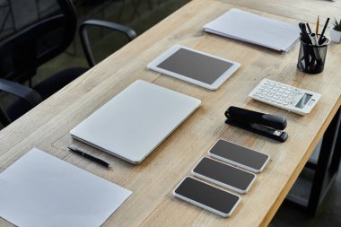Masada bir laptop, tabletler, akıllı telefonlar, kağıtlar ve verimlilik için ofis malzemeleri var..