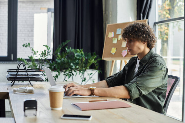 Молодой человек усердно работает на ноутбуке, окруженный яркой атмосферой офиса.