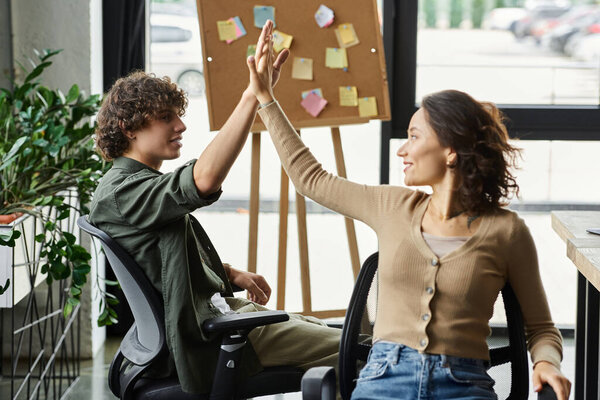 Two colleagues celebrate teamwork with a high five during a productive day at their bright office.
